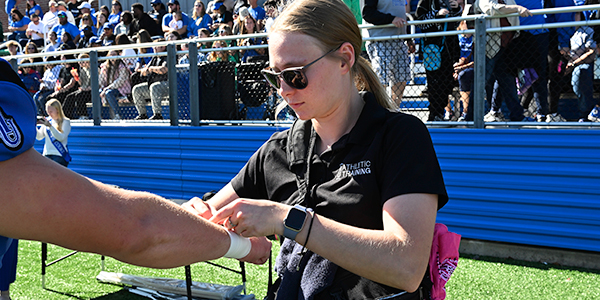 Female Athletic Training student taping an athlete.