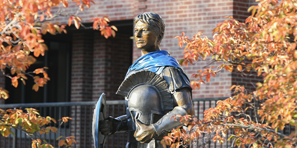 The Spartan Statue overlooks the Quad surrounded by orange leaves in the fall.
