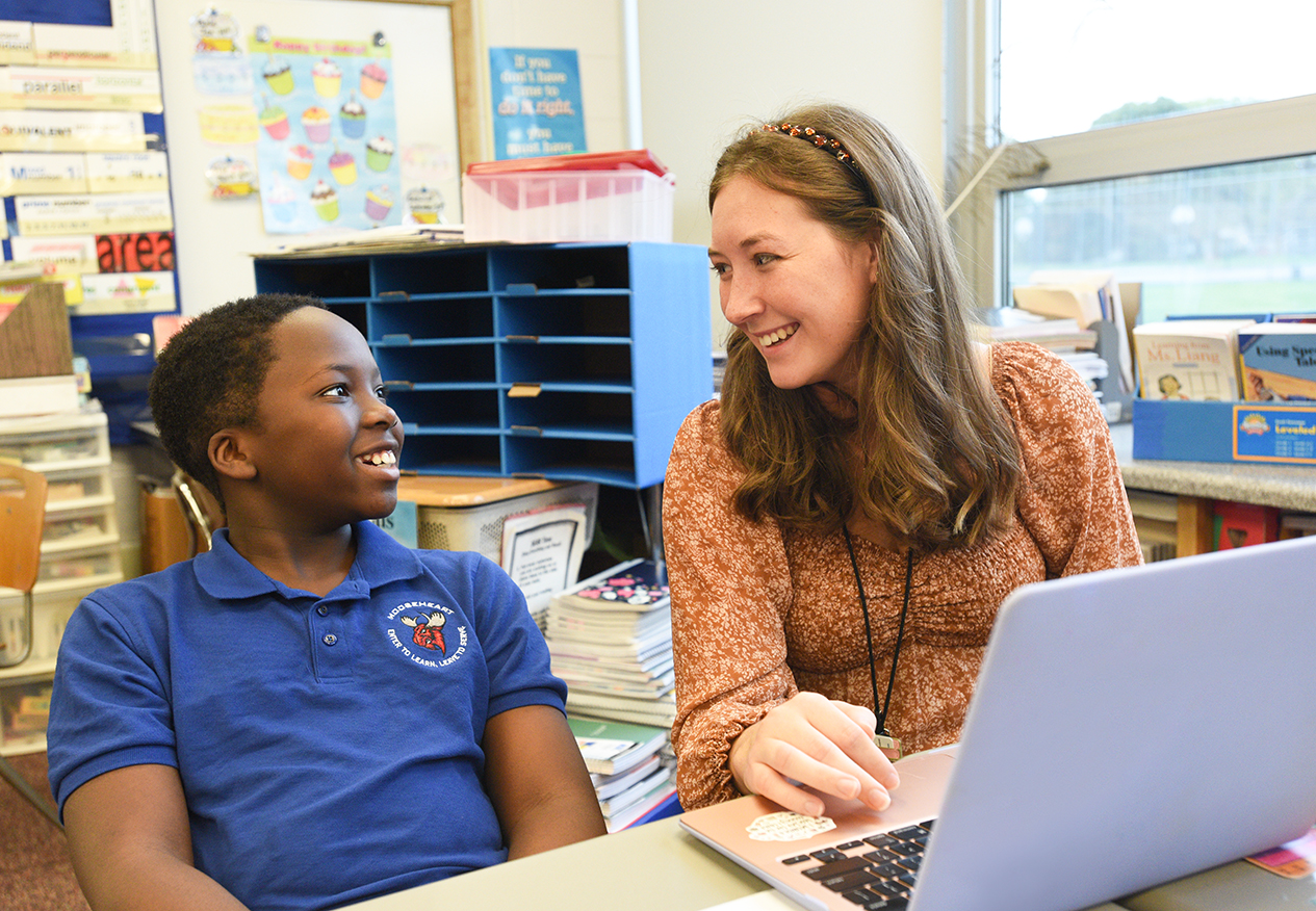 a student teacher assists an elementary school student in a reading room